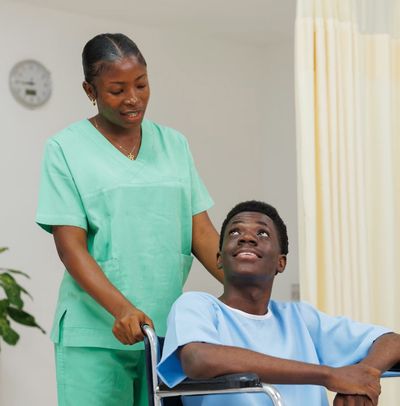 Young man being guided in wheelchair by home health care nursing staff