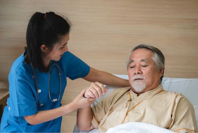 Elderly man being assisted upright in bed by home health professional