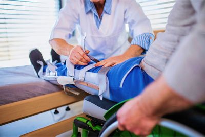 Orthopedic technician helping man in wheelchair put cast on his leg
